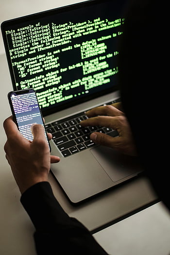 hacker, smartphone, laptop, desk, hooded figure, low light, hacking, coding, computer, technology, cybercrime