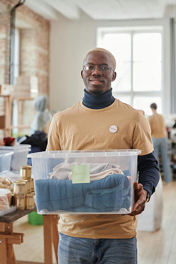 volontario, negozio dell'usato, scatola di donazione, sorridente, uomo nero, contenitore di plastica, carità, servizio alla comunità, volontariato, donazioni, sorriso volontario