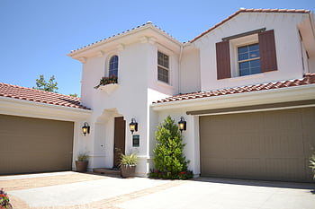 white concrete house, 2-storey house, bright suburban home, classic architecture, landscaped garden, real estate listings, white exterior, brown shutters, tiled roof, garage doors, potted plants
