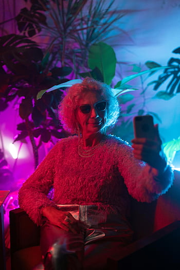 selfie di donna anziana, signora anziana ed elegante, occhiali da sole, illuminazione neon vibrante, piante d'appartamento, autoscatto, luci al neon, moda senior, Elegante anziani, nonna moderna, Atmosfera al neon