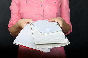 držení notebooků, růžové tričko, prázdné notebooky, tmavé pozadí, hromada notebooků, osoba drží notebooky, tři sešity, spirálové notebooky, vzdělávací potřeby, studijní materiály, kancelářské potřeby