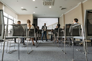Obchodní seminář, Různorodá skupina, mluvčí, Moderní konferenční místnost, obrazovka projektoru, muž stojící, publikum, Profesionální nastavení, prezentace, židle, Okna