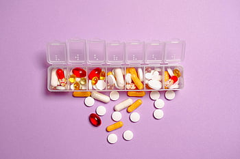 medication pills, white plastic container, daily pill organizer, various pills, capsules, healthcare topics, purple background, pill storage, medication management, health care, pill box