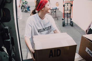 volunteer, woman, white crew neck t-shirt, loading box, charity event, aid boxes, smiling, carrying, charity, volunteer work, donation