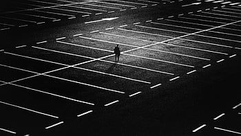 man standing, parking lot, silhouette, solitary figure, expansive, night-time, black and white, urban scene, minimalism, empty space, contrast
