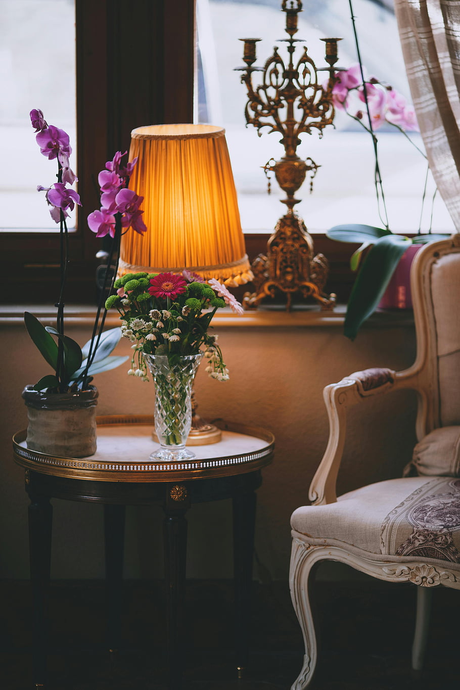cozy living room, floral arrangements, vintage lamp, elegant decor, serene ambiance, room interior, plants on table, decorative chair, window view, soft lighting, vintage candelabra