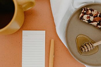 Aufgabenliste, orangefarbene Oberfläche, flach liegen, Kaffeetasse, Nüsse mit Honig, Gemütliches Setup, Oranger Tisch, Honigschöpflöffel, Produktivität, Morgenroutine, Arbeitsbereich Atmosphäre