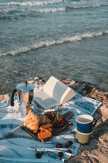 beach picnic, sea waves, coffee, snacks, open book, relaxing beach, picnic setup, beach blanket, cherries, croissants, coffee pot