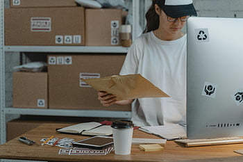 žena, balíček, logistická kancelář, Organizace pracovního prostoru, Efektivní pracovní prostor, třídění balíků, lavice, kávový šálek, laptop, samolepící papírky, kancelářské potřeby