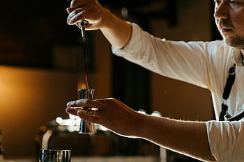 bartender, uniform, measuring spirits, jigger, dimly lit, indoor bar, expertly, bar setting, cocktail preparation, professional bartender, barman