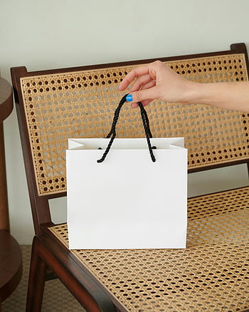 pessoa segurando bolsa de papel, bolsa de papel branco, Cadeira de madeira tecida, Configuração interna minimalista, alcance da mão, configuração interna, design minimalista, saco de papel, cadeira tecida, decoração minimalista, Foto interna