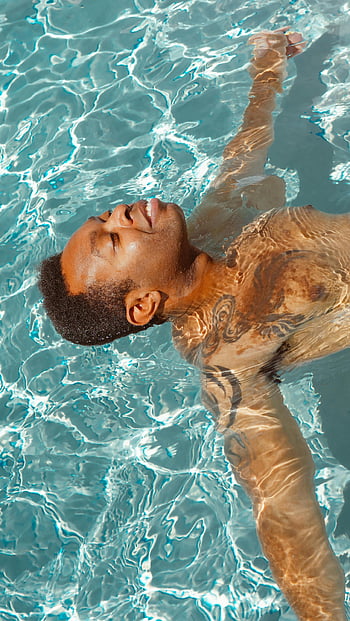 man relaxing, swimming pool, peaceful float, sunbathing, sparkling pool, summer day, man in pool, water ripples, outdoor relaxation, tattooed man, poolside leisure