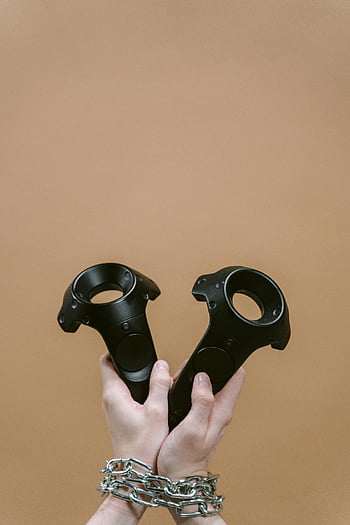 Gamecontroller, schwarze Controller, Hände gebunden, Ketten, brauner Hintergrund, Spielzubehör, Virtual -Reality -Controller, Handfesseln, einzigartiges Gaming-Setup, Controller -Design, Gaming -Ausrüstung