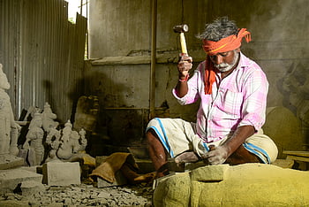 man holding hammer, skilled artisan, crafting stone sculpture, traditional workshop, stone carving, artisan tools, workshop setting, cultural craft, traditional artistry, stone sculpture, artisan work
