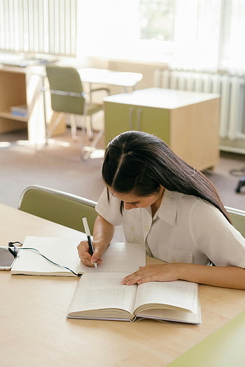 Kvinna som studerar, bibliotek, ung kvinna, skriva anteckningsbok, studiebord, bibliotekstabell, bok, penna, fokuserad student, akademisk miljö, inlärning