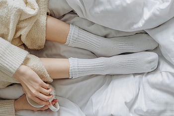 white socks, ceramic cup, relaxing indoors, white linens, warm clothing, soothing moment, cozy scene, indoor relaxation, comfort, soft textures, home comfort