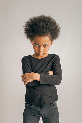 Nevrhavá černá dívka, zkříženýma rukama, rozzlobený výraz, příležitostné černé oblečení, mladá dívka, afro vlasy, u zdi, portrét, studio shot, fotografování v interiéru, černé oblečení