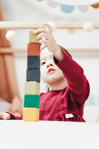young girl, red dress, building blocks, indoor playroom, colorful wooden blocks, selective focus, child playing, stacking blocks, playtime, early childhood, educational toys
