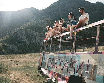 abandoned bus, group of people, young adults, colorful bus, mountain setting, peaceful setting, outdoor adventure, travel photography, nature backdrop, abandoned vehicle, graffiti art