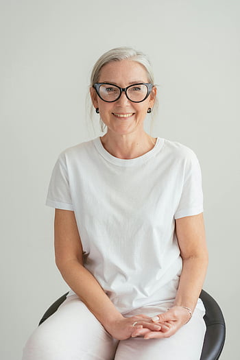 starsza kobieta, Biała koszulka, okulary, uśmiechnięty, wewnątrz, portret, szczęśliwy, Zwyczajny outfit, czarne krzesło, naturalne światło