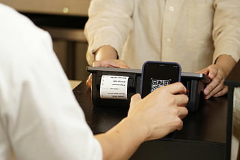 QR code, contactless payment, retail counter, QR code scanner, close-up shot, mobile payment, two individuals, payment process, digital transaction, smartphone scanning, retail transaction
