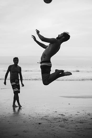 Beach-Volleyball, Nackter Oberkörper Mann, springen, Fußball, Freizeit am Meer, Dynamischer Schuss, Sportlichkeit, Strandaktivität, zwei Männer, Schwarz und weiß, Ozean Hintergrund