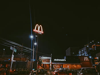 McDonald's, nighttime, city setting, neon signage, brightly lit, restaurant, urban scene, drive-thru, street lights, building exterior, cars parked
