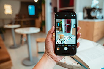 Person, die Telefon hält, Schwarzes Handy, Modernes Café, Kaffee fotografieren, Smartphone, Café -Einstellung, Kaffee Foto, modernes Interieur, Cafe Interieur, Hand, die Telefon hält, Kaffeetasse
