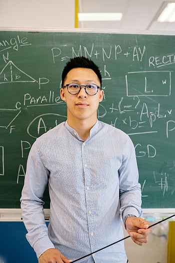 male teacher, blue long sleeve shirt, looking at camera, Asian male teacher, mathematical equations, blackboard, confident pose, classroom setting, educational environment, teaching profession, glasses