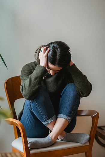 anxious young woman, covering ears, hands, sitting on chair, indoor, distress, emotional stress, mental health, casual clothing, gray socks, wooden chair