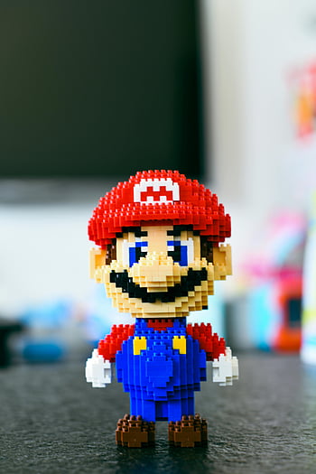 Super Mario, mini building blocks, pixelated toy, video game character, blurred background, LEGO figure, Mario figure, building block art, pixel art, toy figure, Mario toy