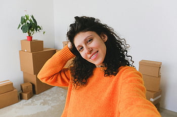 nieuw appartement, verhuizing, vrolijke vrouw, Verhuisdozen, selfie, tevreden jonge vrouw, glimlachende vrouw, oranje trui, kamerplant, verhuisdag