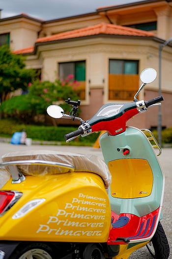yellow Vespa, red and yellow scooter, parked scooter, residential street, urban lifestyle, Primavera scooter, vibrant scooter, street parked scooter, Vespa Primavera, scooter on street, colorful scooter