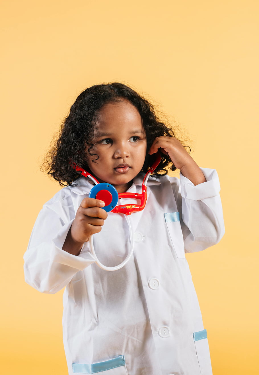 black girl, medical robe, toy stethoscope, cute child, dressed as doctor, yellow background, playing doctor, child doctor, medical play, young doctor, toy doctor