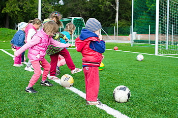 batole hraje fotbal, děti hrají fotbal, Venkovní fotbal, slunečný den, park, děti si hrají, fotbalové míče, travnaté hřiště, malé děti, sportovní aktivity, zábava venku