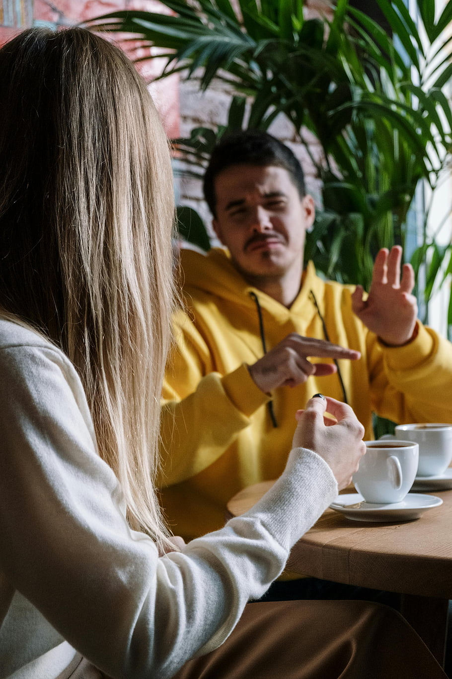 man, woman, sign language, hand gestures, coffee, cozy cafe, communication, interaction, yellow hoodie, white sweater, indoor setting