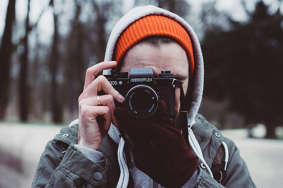 man, gray hooded jacket, black camera, winter coat, beanie, forest setting, taking photos, outdoor photography, casual attire, nature photography, winter scene
