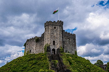 Cardiff Castle, Wales, old castle, cloudy sky, dramatic sky, flag, historic architecture, medieval castle, green hill, stone structure, Welsh flag