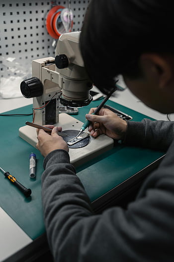 soldering iron, microchip, microscope, electronics lab, technician, focused work, electronic repair, soldering process, precision work, lab equipment, microelectronics