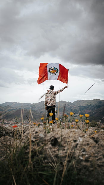 man, mountain peak, Peru flag, overcast sky, Peruvian mountains, flag waving, outdoor adventure, scenic view, nature landscape, travel photography, patriotic moment