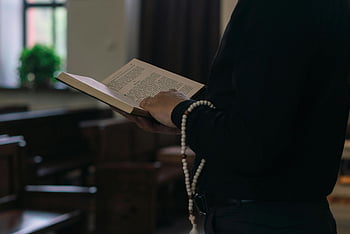 osoba v černé barvě, dlouhé rukávy, držení Bible, modlitební korálky, interiér kostela, duchovní prostředí, náboženská scéna, Svatá kniha, modlitba, víra, oddanost