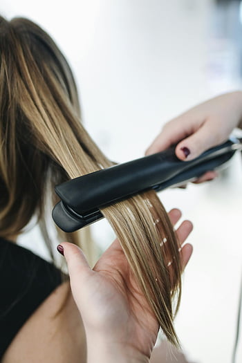 hairstylist, flat iron, blonde hair, salon setting, close-up, hair styling, hair straightening, beauty treatment, professional hairstyling, hair care, salon services