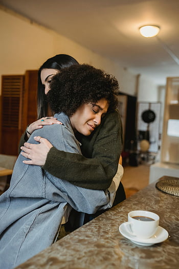 troostende omhelzing, zwarte vriendin, oprecht moment, ondersteuning, kop koffie, twee vrouwen, Emotionele band, aardige vrouw, binnenomgeving, koffietafel, comfort