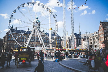 Ferris wheel, brown buildings, people, blue cloudy sky, city carnival, giant Ferris wheel, blue sky, daytime, lively day, city scene, amusement park