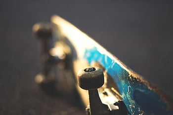skateboard, modré a bílé, betonová podlaha, mírně nakloněné, Umělecké detaily, skateboardová kola, rozmazané pozadí, Zachycení slunečního světla, detailní fotografie, městské sporty, venkovní aktivita