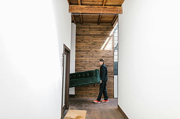 man carrying sofa, green sofa, modern hallway, wooden hallway, relocation service, moving service, mover, indoor moving, furniture moving, green couch, modern interior