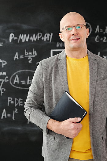man-in-gray-blazer-holding-notebook-smiling-teacher-classroom-blackboard-equations-education-teaching-mathematics-professional-academic-thumbnail.jpg