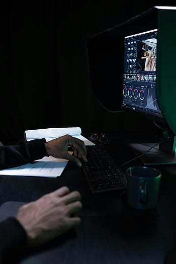 video editor, color grading, dimly lit room, computer, close-up, workspace, keyboard, monitor, editing software, hands typing, mug