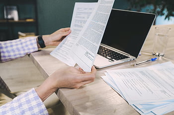 Person, die Papiere hält, weiß gedruckte Dokumente, Nahaufnahme Hände, Untersuchung von Dokumenten, Schreibtisch, Laptop, gedruckte Papiere, Arbeitsumgebung, Geschäftseinstellung, Überprüfung der Dokumente, Büroarbeitsplatz