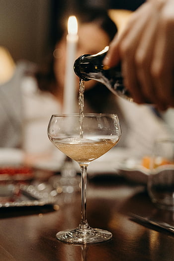 champagne, coupe glass, pouring champagne, candlelit dinner, shallow focus, close-up, wine glass, dining setting, elegant drink, celebration, bubbles